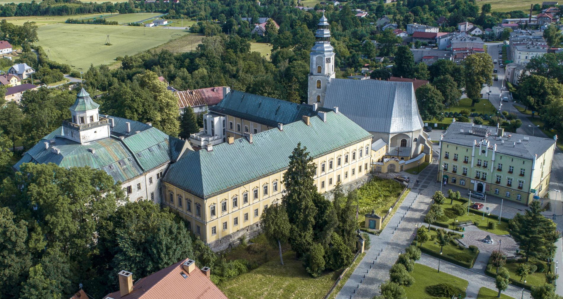 Widok na zamek z lotu ptaka, zielony dach, żółta elewacja. Wokół drzewa.