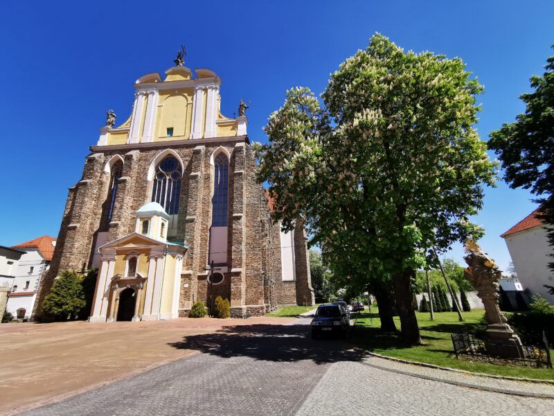 Zdjęcie przedstawia kościół z szarych cegieł, niektóre części pokryte są żółto-białą elewacją.