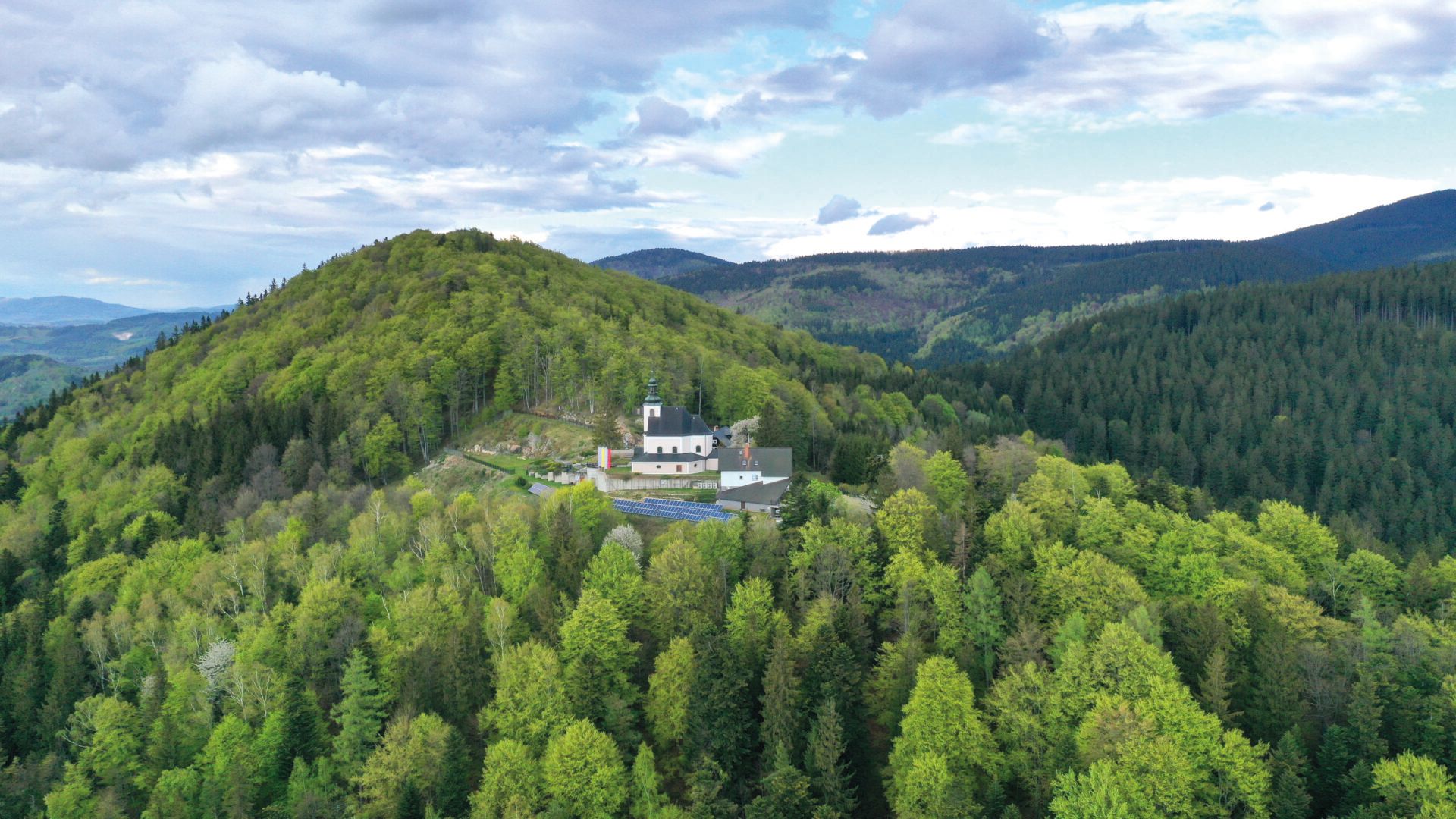 Widok z lotu ptaka na położone na zboczu góry zabytkowe sanktuarium w otoczeniu zielonych koron drzew i gór