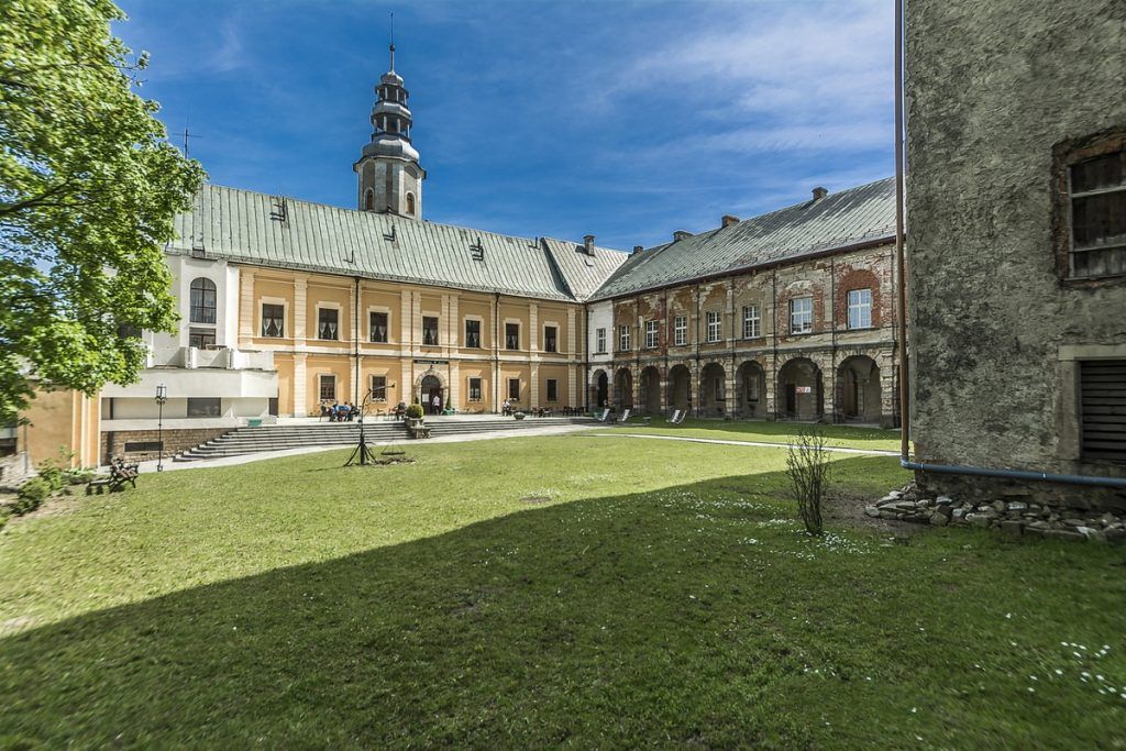 Na pierwszym planie zielona trawa, widoczna część zamku z nową elewacją, żółtą z białymi akcentami. Widać część zamku nieodrestaurowana.