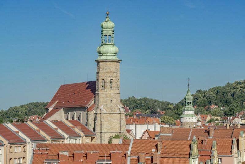 Widok z góry, na ratusz oraz budynki wokół niego. W tle lasy oraz błękitne niebo.