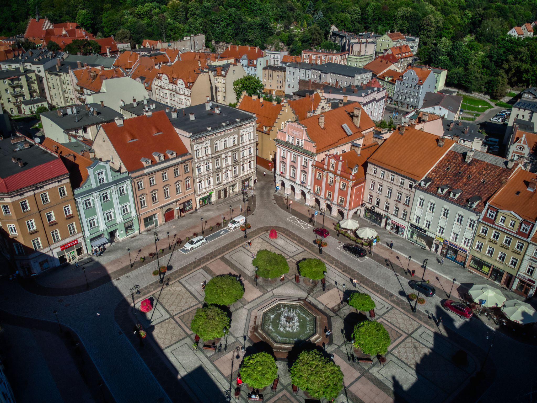 Zdjęcie z Drona przedstawiające stare zabytkowe kamienice, których pośrodku znajduje się zadbany plac z liczną zielenią, drzewami