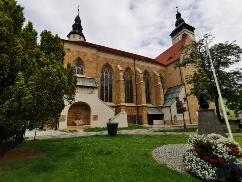 Gotycka budowla z potężnymi przyporami i strzelistą wieżą, zwieńczoną hełmem.