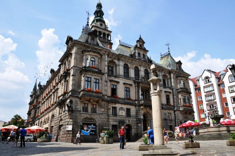 Widok na kłodzki ratusz, budowla w stylu neorenesansowym, wyróżniająca się smukłą wieżą zegarową oraz bogato zdobioną fasadą z detalami architektonicznymi.