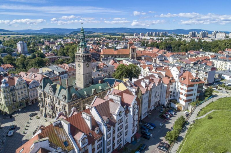 Widok ze szczytu góry na zabudowę Kłodzka z widocznymi szcytami gór w tle