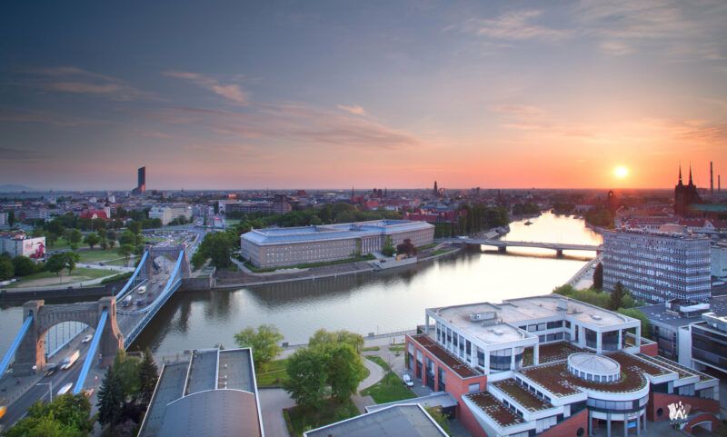Widok z lotu ptaka na szerokie koryto rzeki Odry oraz zabudowania miasta wrocław na tle zachodzącego słońca