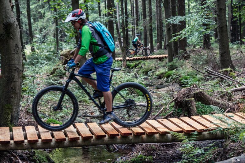 Rowerzyści przejeżdzają przez drewniane pomosty.