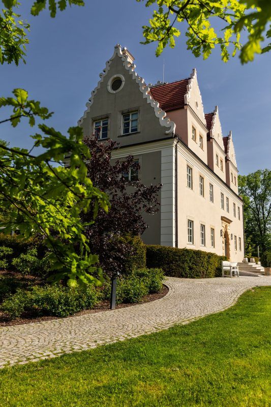 Zamek Topacz, widoczny z zewnątrz, to majestatyczna budowla o bogatej historii, której eleganckiej mury odbijają się w spokojnych wodach otaczającego go parku.