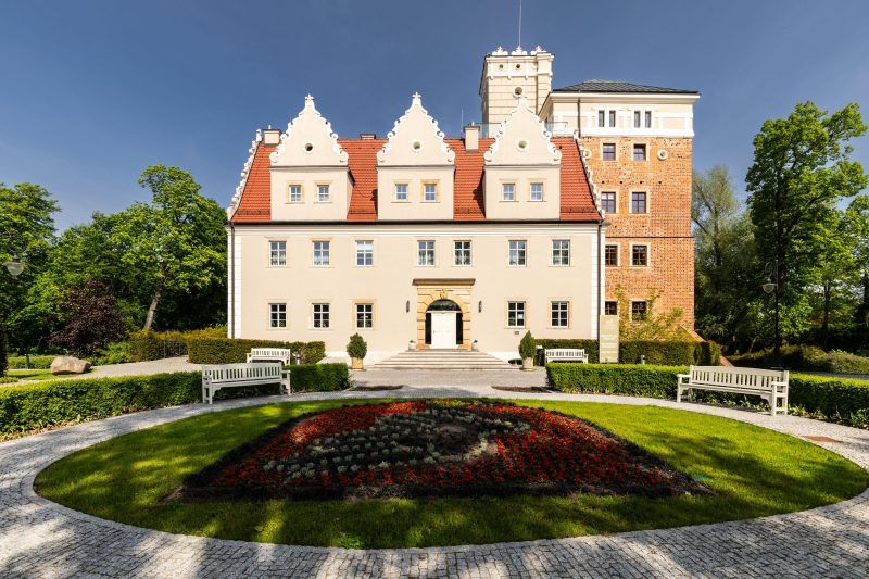 Główne wejście do zamku Topacz to imponująca brama z wieżą obronną, prowadząca na dziedziniec, otoczona murami i ozdobiona kamieniarskimi detalami.