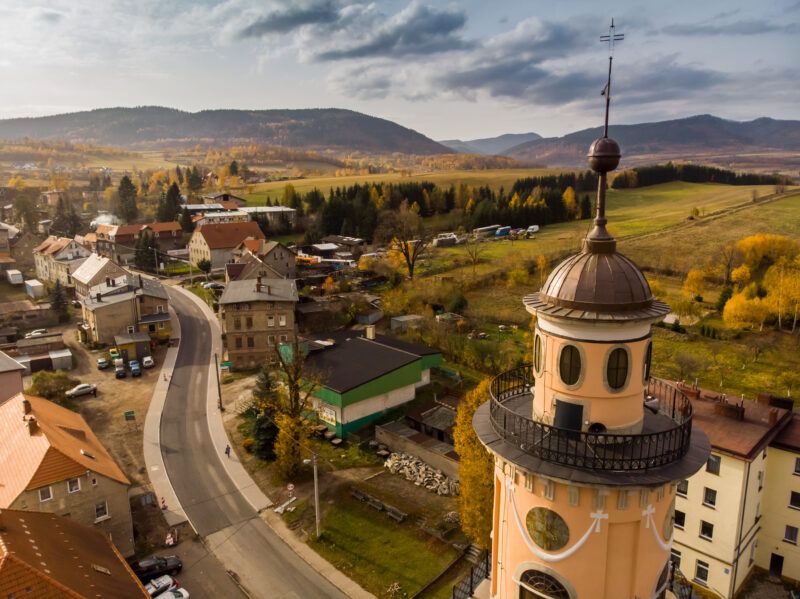 Zdjęcie z lotu ptaka na zabudowę głuszycy z widoczną wieżą ratuszową lub kościelną na pierwszym planie i z górami w tle