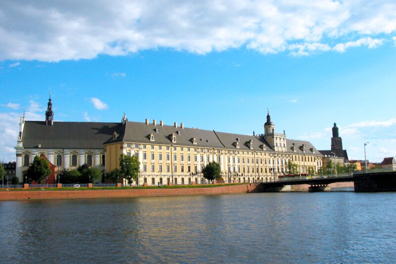 Widok na rzekę, w tle długi budynek z żółtymi akcentami.