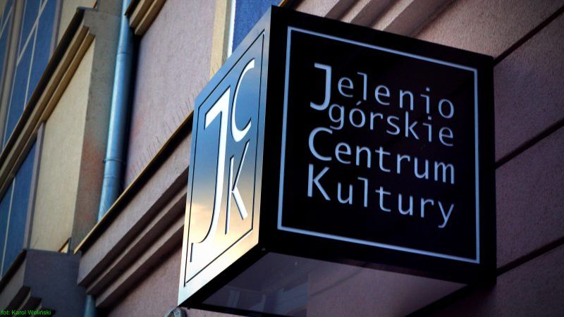 Zdjęcie przedstawia czarny szyld z białymi napisami na elewacji budynku