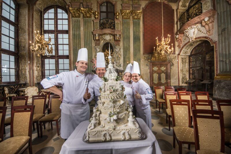 Zdjęcie tortu z trójką kucharzy w kuchennych strojach zrobione w pięknej barowej sali zamkowej