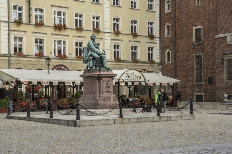 widok na zadaszony ogródek należący do Restauracji Pod Fredrą, kamienicę oraz pomnik 