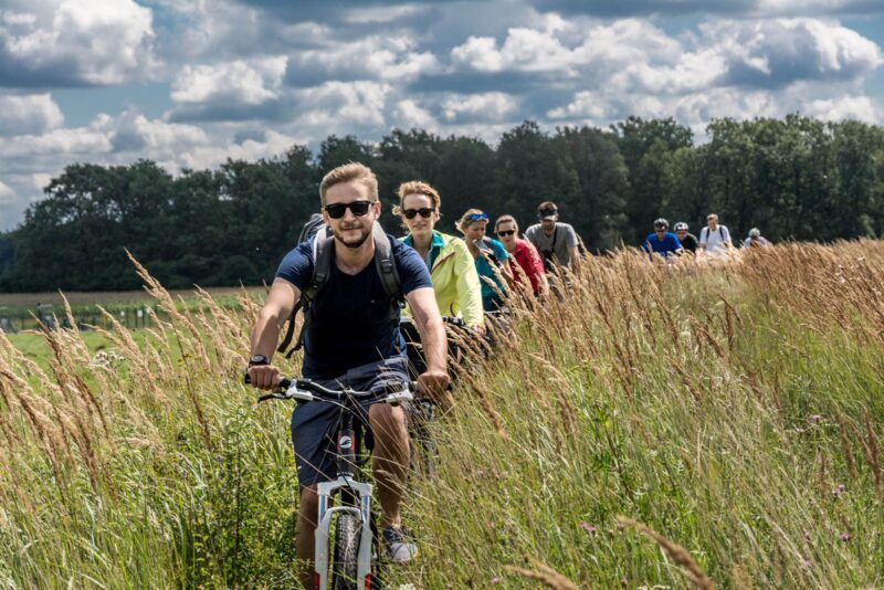 Grupa rowerzystów podczas jazdy przez zarośla widziana od frontu na tle zachmurzonego nieba