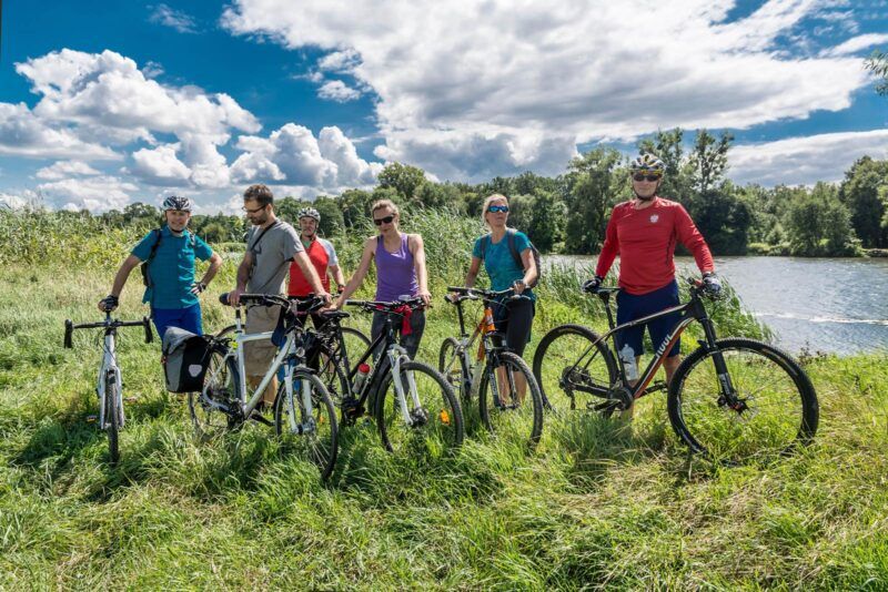 Grupa rowerzystów pozuje na tle roślinności oraz Odry