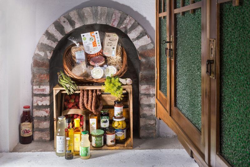 Przez otwarte okno w zabudowanej cegłami ścianie artystycznie ułożone produkty regionalne tworzące spójną wystawę z wielu różnych składników spożywczych.  