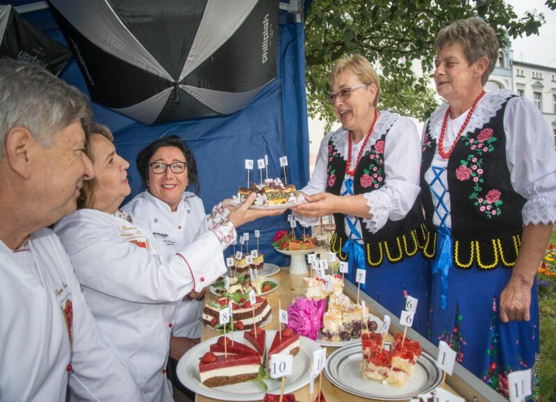 Zdjęcie grupy ludzi w ludowych strojach przy stole z daniami konkursowymi