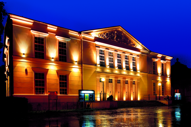 Zdjęcie przedstawia klasycystyczny budynek teatru w Jeleniej Górze ze sztucznym oświetleniem fasady na tle wieczornego nieba
