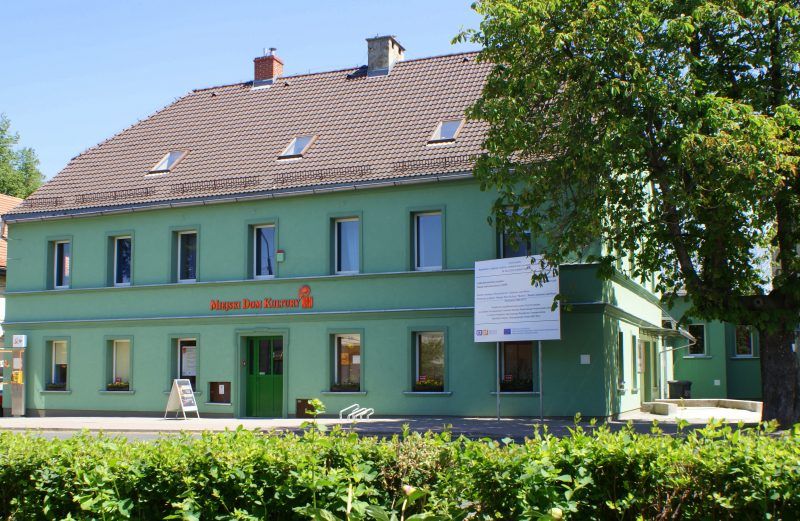 Zielony budynek z czerwonym dachem, w którym znajduje się dom kultury