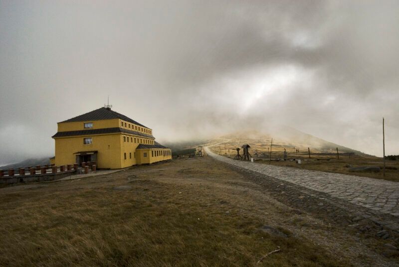 Brukowana droga prowadząca do schroniska górskiego. W tle szczyt, przysłonięty przez niskie chmury.