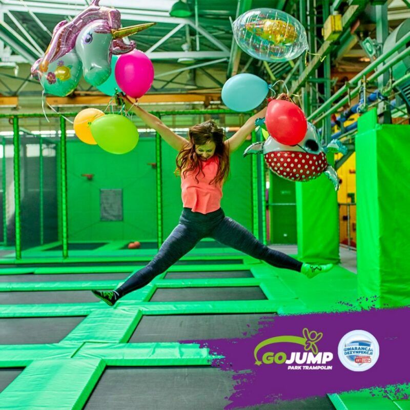 Dziewczynka podskakuje na trampolinie trzymając baloniki