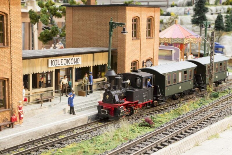 Makieta pociągu parowego z wagonami na tle miniatury stacji kolejowej z podpisem Kolejkowo