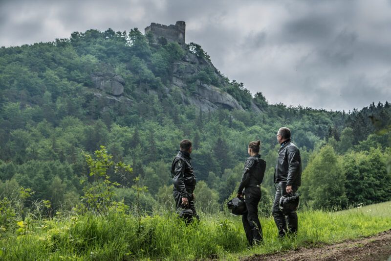 Widok z dołu ma kamienny zamek ustawiony na skalistej góry. W tle błękitne niebo.