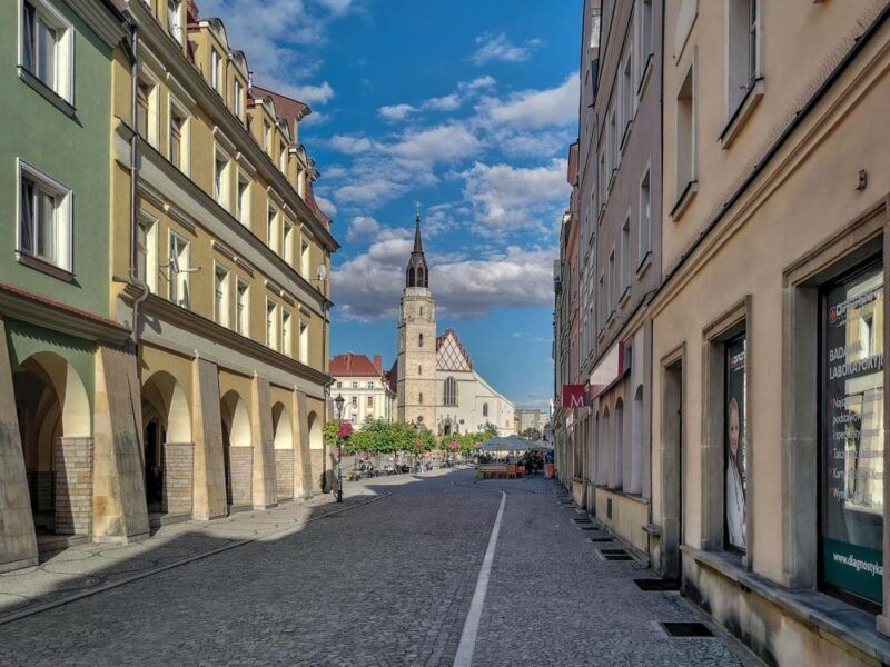 Widok na budynek z wysoką wieżą. Znajduje się na końcu ulicy, pomiędzy kamienicami.