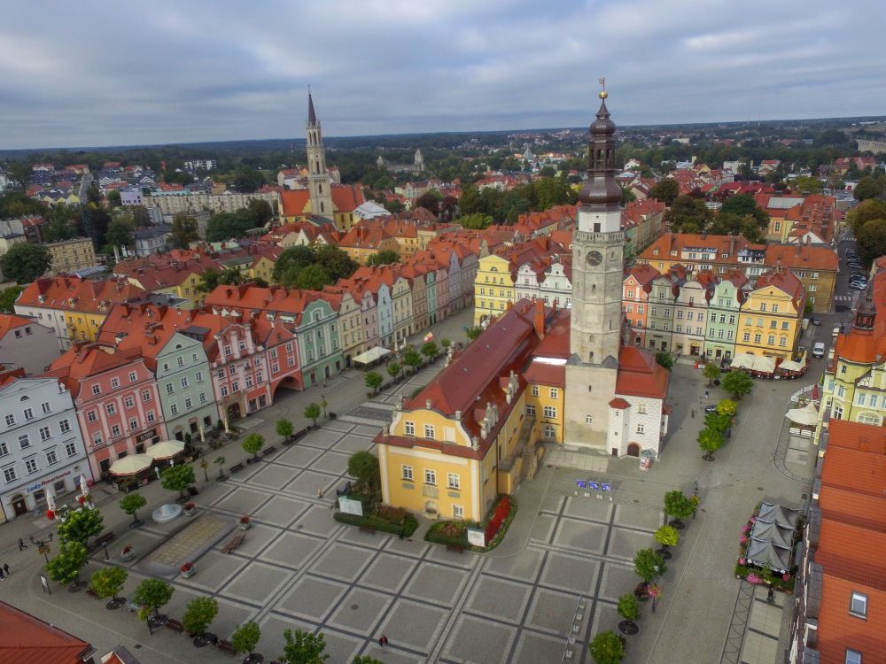 Widok z góry na rynek w Bolesławcu. Kolorowe kamieniczki, odrobina zieleni miejskiej, w centrum budynek ratusza.