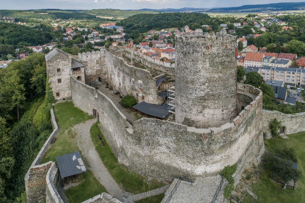 Majestatyczne ruiny średniowiecznej warowni z widocznym systemem murów zewnętrznych, podgrodziem oraz masywną wieżą obronną.