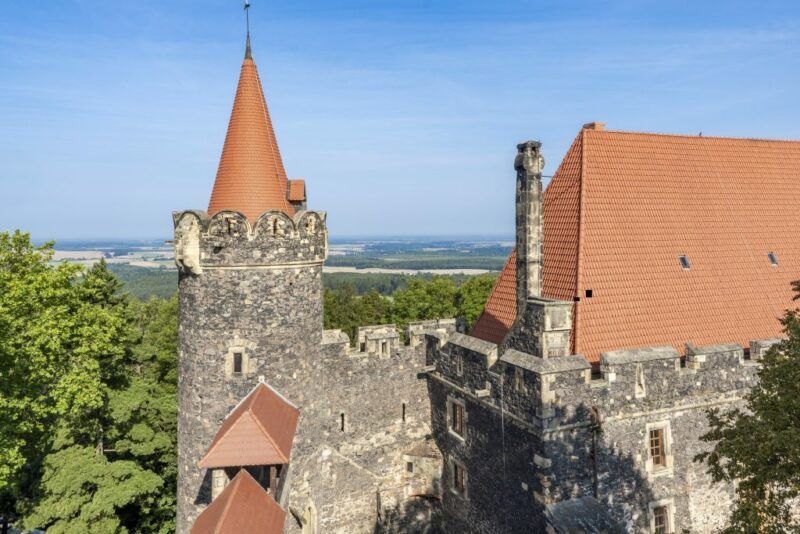 Widok na wieżę kamiennego zamku pokrytą dachem z dachówką na tle błękitnego nieba