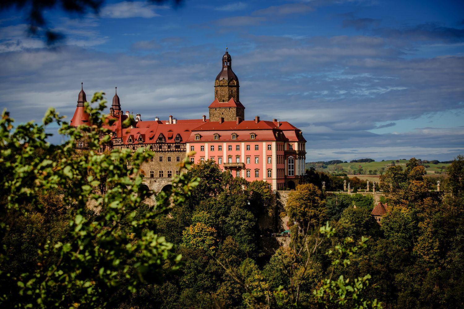 Zamek Książ wśród roślinności. Widok z oddali (z punktu widokowego na skarpie) na bok zamku.