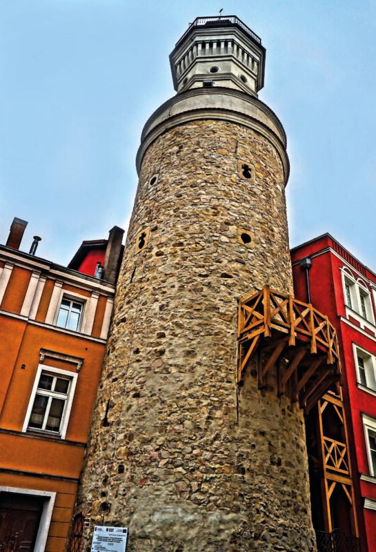 Kamienna, nieotynkowa wieża widokowa na planie kołą z widoczną drewnianą platformą na boku.