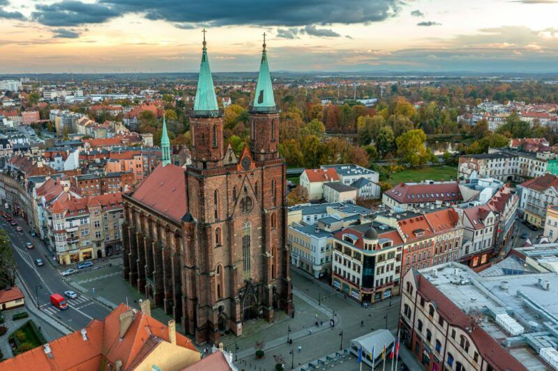 Panorama miasta- zabytkowy kościół ewangelicki z dwoma wieżami, w tle park miejski a naokoło budynki z ceglanymi dachami