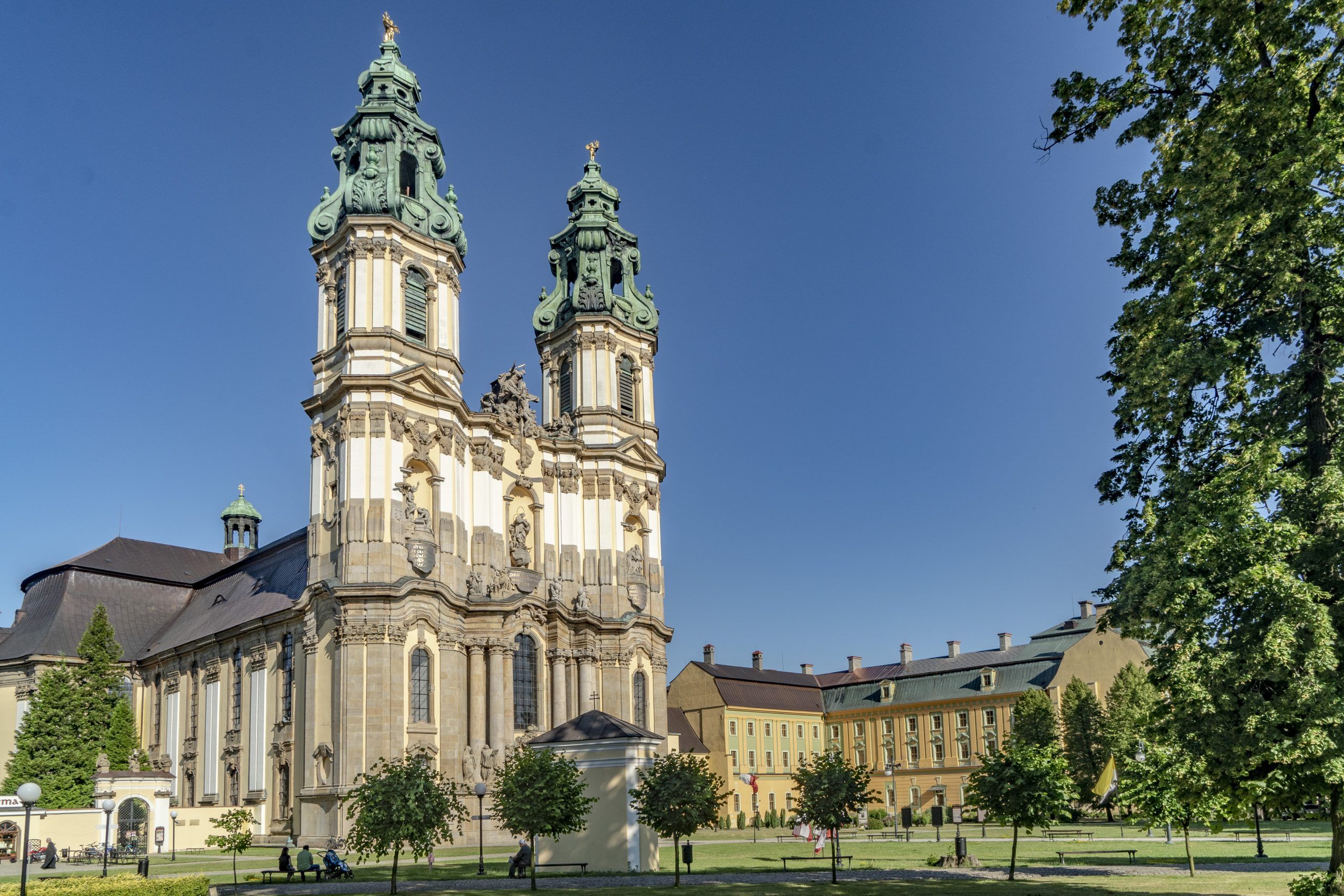 Dwie wysokie wieże  kościelne w stylu barokowym, obok zabytkowe żółte budynki opactwa