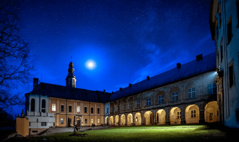 Widok na zamek nocą, w tle niebo z jasno świecącym księżycem.