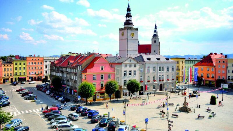 Widok na skąpany w słońcu rynek w Dzierżoniowie z widocznym blokiem śródrynkowym i masywną, kwadratową w swym planie wieżą ratuszową.