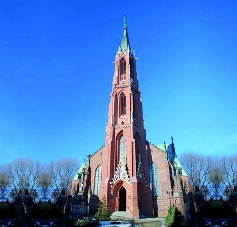 Widok na strzelistą, ceglaną, neogotycką wieżę kościelną na tle błękitnego nieba