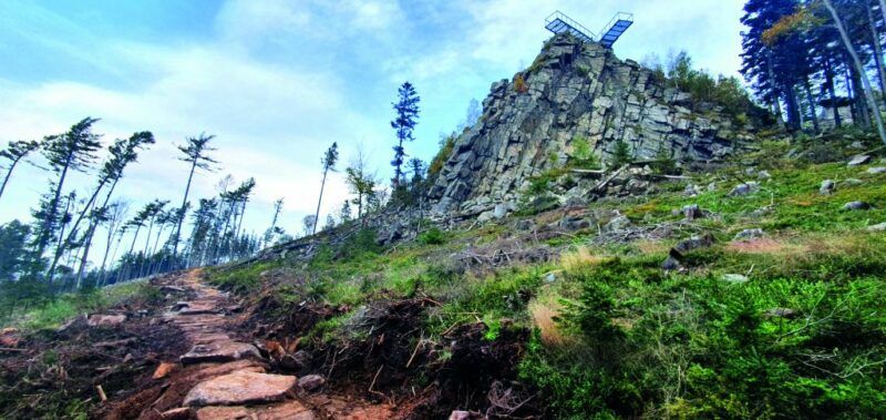 Widok na metalowy pomost-platformę od strony podejścia do wzniesienia. Platforma znajduje się na kamiennym ostańcu