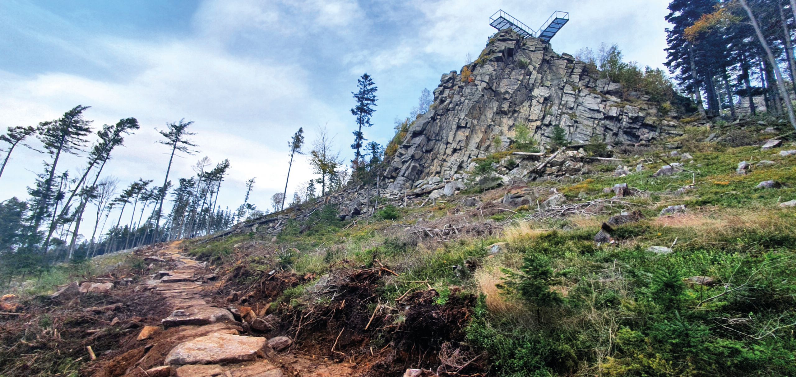 Widok na metalowy pomost-platformę od strony podejścia do wzniesienia. Platforma znajduje się na kamiennym ostańcu