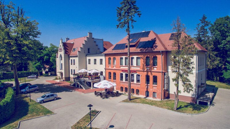 Budynek w kolorach czerwonym i biały z czerwonym dachem w otoczeniu drzew z szeroką drogą podjazdową
