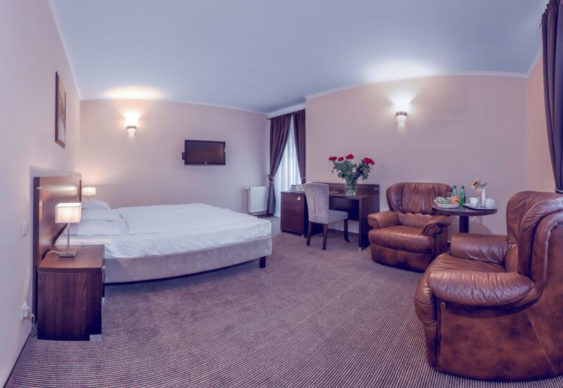 Pokój hotelowy wyposażony w fotele łóżko wykładzinę trzy lampy oświetlające pomieszczenie.