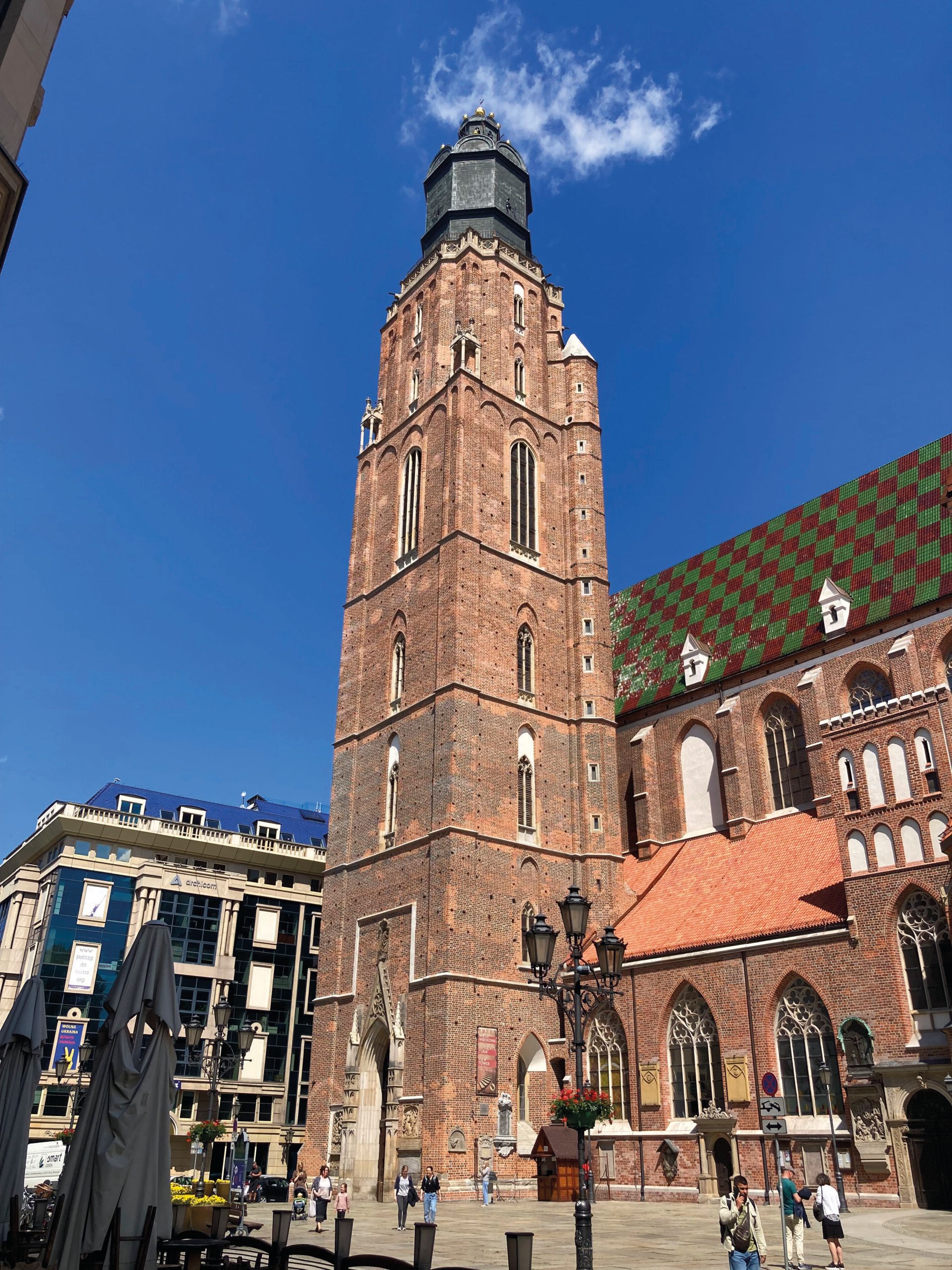 Widok z poziomu ulicy na oświetloną promieniami słońca ceglaną, prawie 100-metrową, kwadratową w swym planie wieżę kościoła farnego św. Elżbiety we Wrocławiu