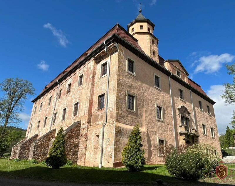 Zrewitalizowana elewacja bocznej fasady trójkondygnacjnego budynku pałacu na tle błękitnego nieba.