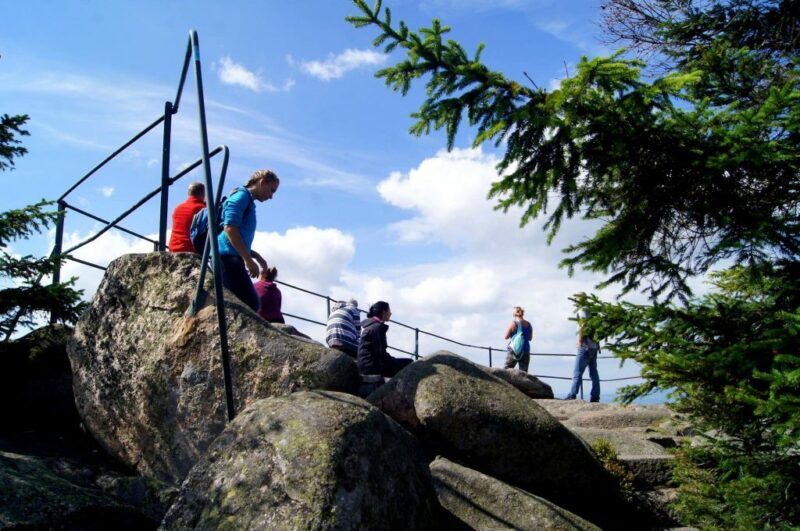 Widok na turystów podziwiających widoki z kamiennej platformy widokowej z metalowymi barierkami na tle błękitnego nieba