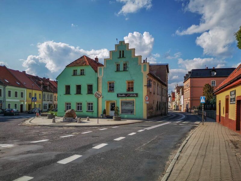 Zielone kamienice pomiędzy dwoma asfaltowymi drogami.