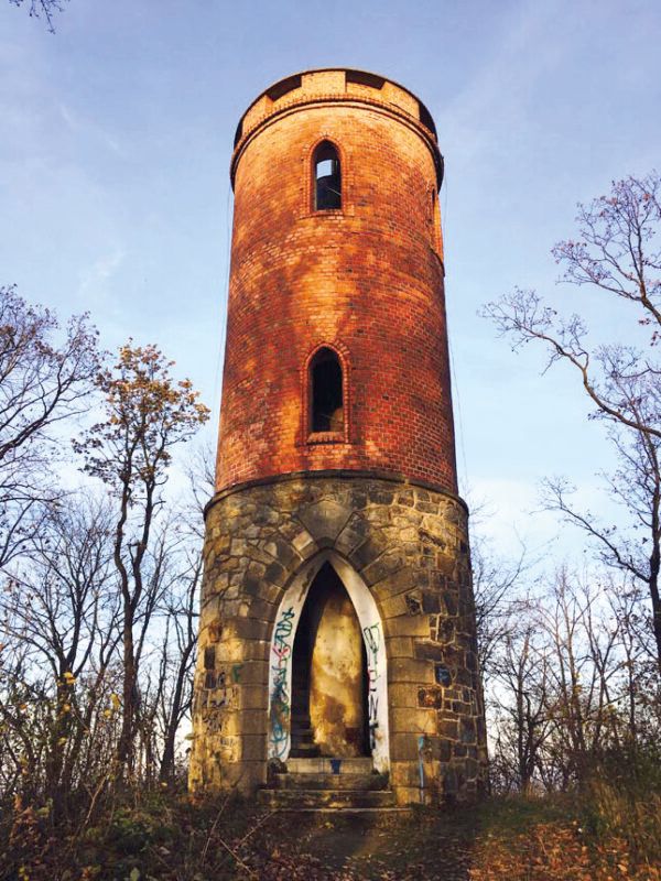 Jesienny widok z poziomu gruntu na zabytkową kamienno-ceglaną wieżę widokową na tle nieba