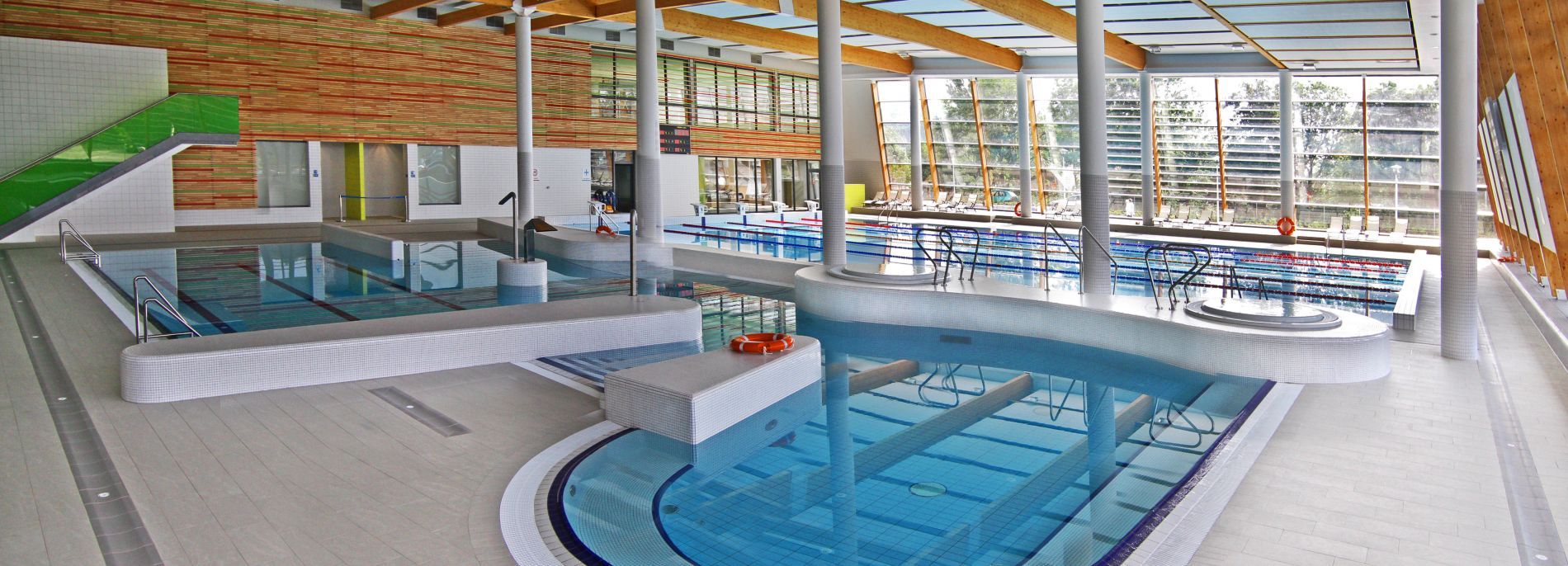 Trzy niecki basenowe w części sportowo-rekreacyjnej hotelu. Przeszklone ściany i elementy drewniane.