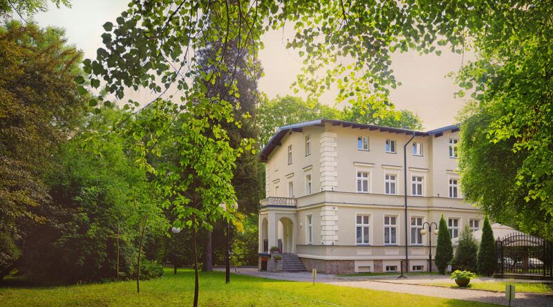 Widok na budynek uzdrowiska w otoczeniu bujnej przyrody.